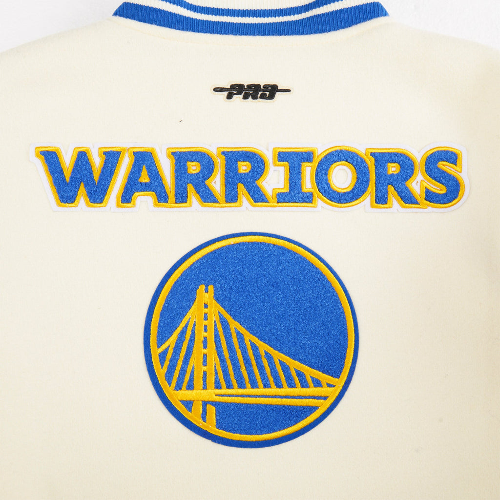 NBA GOLDEN STATE WARRIORS CLASSIC STUDIO BLOUSON COLLÉGIAL POUR GARÇON JUNIOR (COQUILLE D'ŒUF/BLEU ROYAL)